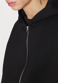 Black hooded sweatshirt featuring a smooth fabric texture, a front zipper closure, and a modern design with a contoured collar.