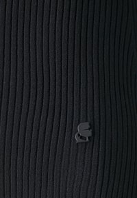 Μαύρο ριγέ παντελόνι κολάν με μικρή μαύρη ετικέτα λογότυπου. Η υφή είναι ομαλή με συνεπείς κατακόρυφες ραβδώσεις σε όλη την επιφάνεια.