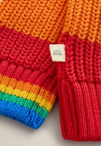 Capo lavorato a maglia di colore rosso con strisce orizzontali arancioni, gialle, verdi e blu. Presenta un motivo testurizzato e una piccola etichetta di stoffa con un design arcobaleno.