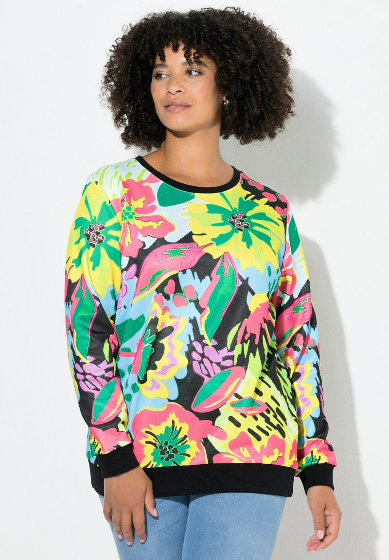 Sweatshirt floral coloré avec des motifs roses, jaunes et verts sur un fond noir ; poignets et encolure noirs côtelés, coupe ample.