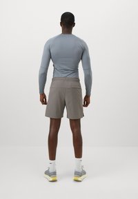 Langærmet, tætsiddende grå skjorte parret med løse, knælange brune shorts. Sættet har en elastisk talje og glatte teksturer.