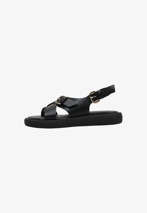 Sandale plate noire avec deux boucles dorées, bout ouvert et bride arrière pour le maintien de la cheville, présentée sur un fond blanc.