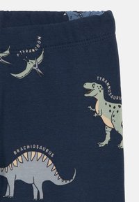 Leggings in cotone blu navy con stampe di dinosauri, tra cui Tyrannosaurus e Brachiosaurus. Texture liscia con una vita elastica.