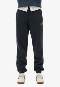 Navyblauwe katoenen joggingbroek met een taps toelopende pasvorm, elastische boorden en een subtiele "Superdry"-logo in goud aan de linkerkant.