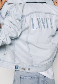 Giacca in denim azzurro chiaro con maniche lunghe, colletto e logo Levi's ricamato sul retro. Include chiusura con bottoni e tasche.