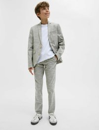 Ljusgrå linnekostym med en texturerad yta, som har en enknappad blazer och matchande byxor, i kombination med en vit t-shirt och sneakers.