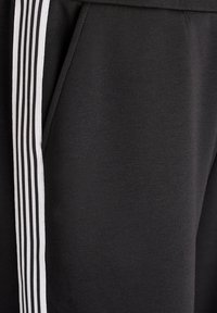 Black sweatpants with a smooth texture, featuring a white triple stripe detail along the side and a side pocket.