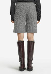 Hellgraue gestrickte Shorts mit einem Kabelmuster, gerippten Säumen, kombiniert mit glänzenden bordeauxfarbenen knielangen Stiefeln mit einem stabilen Absatz.