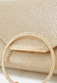 Borsa a pochette dorata con una superficie testurizzata decorata con piccole perline, un manico circolare adornato con strass e un logo impresso.