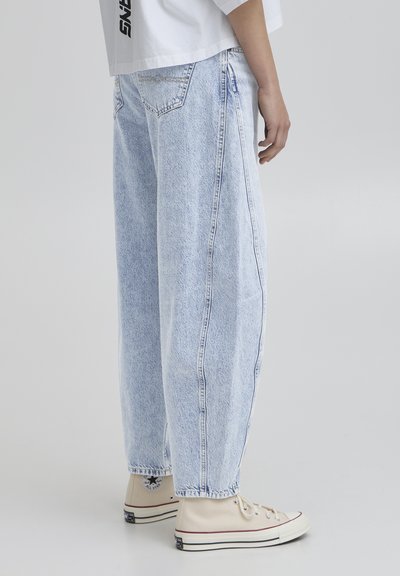 Svijetloplavi, široki traperice s blagim izblijedjelim teksturom i vidljivim šavovima, uparene s bež platnenim tenisicama.