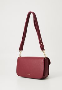 Burgundy leather handbag with a structured shape, gold hardware, and an adjustable strap; features a textured finish with a flap closure.