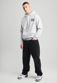 Light gray hooded sweatshirt with "USA" graphic, front pocket, paired with black pants and white sneakers featuring gray accents.