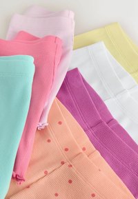 Leggings côtelés pliés en rose pastel, corail à pois, vert menthe, violet, blanc et jaune, disposés sur une surface claire.