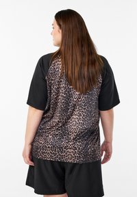 Camiseta negra de manga corta con espalda de estampado de leopardo, presenta un ajuste relajado y textura ligera, combinada con pantalones cortos negros.