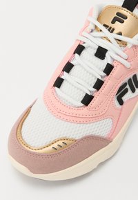 Baskets blanches à lacets avec accents roses, dorés et beige clair. Comprend une tige en maille, un col rembourré et des détails texturés sur la semelle.