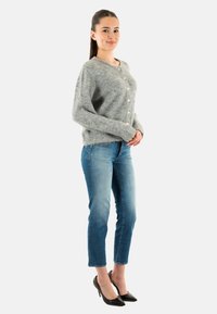 Cárdigan gris de punto con cuello redondo y cierre de botones, combinado con jeans de color azul claro y tacones de punta negra.