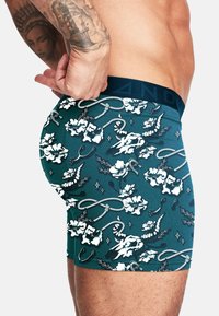 Herrens boxertrosor i teal med ett blommönster och repmönster, tillverkade av stretchigt tyg, med en svart midjeresår med logodetalj.