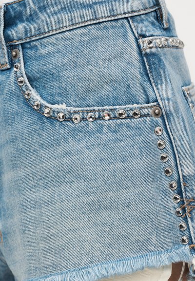 Φωτεινά μπλε τζιν σορτς με ξεφτισμένο τελείωμα και ασημένιες στολισμένες τάπες κατά μήκος των τσεπών και των πλαϊνών ραφών.