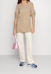 Maglione beige a maglia, vestibilità ampia, polsini a coste, abbinato a pantaloni in corduroy crema. Borsa a tracolla a quadri rosa e sneakers blu/neri.