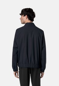 Giacca bomber blu navy con colletto, orlo ed elastici alle maniche. Caratterizzata da un tessuto liscio e leggero e da un design minimalista.