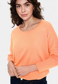 Leichtes orangenes Strickpullover mit weitem Halsausschnitt und langen Ärmeln. Die Textur ist glatt mit Rippenstruktur an den Bündchen und dem Saum.