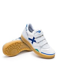 Zapatillas deportivas blancas con acentos azules, correas de gancho y bucle, suela de goma texturada y parte superior sintética suave. Presentan un patrón de diseño único.