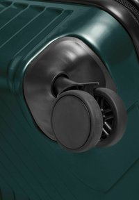 Ruote a doppio spinner nere collegate all'angolo di una valigia rigida verde scuro.