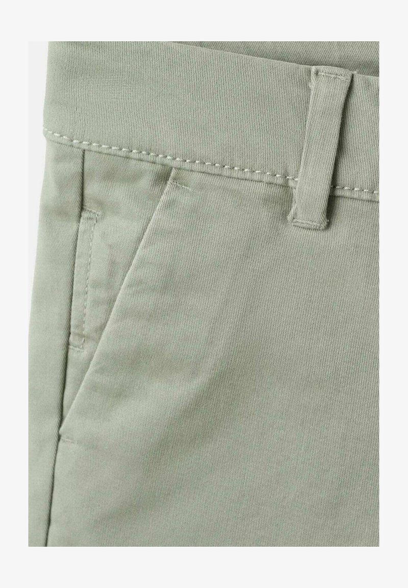 Gros plan sur un pantalon gris clair montrant la poche avant, la passants de ceinture et les détails de couture de la ceinture.
