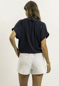 Haut bleu marine à manches courtes avec une coupe ample et des poignets retroussés, associé à un short blanc. Texture lisse, sans motifs visibles, design simple.