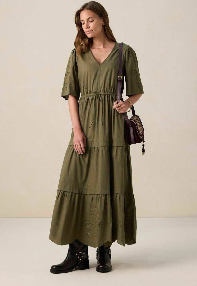 Robe en coton vert olive, longueur genou, avec un décolleté en V, des manches bouffantes et une taille à cordon. Elle présente une jupe à volants et des broderies.