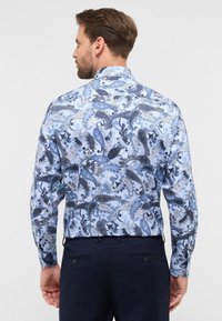 Een overhemd met knopen in een lichtblauwe basis, een ingewikkeld marineblauw en wit paisleypatroon, en lange mouwen. Het heeft een standaardkraag en een rechte snit.