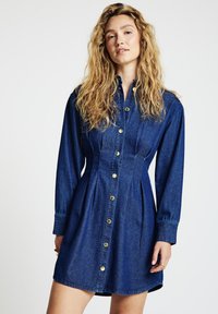 Jeanskleid mit knöpfbarer Vorderseite, goldenen Beschlägen, langen Ärmeln, tailliertem Schnitt und plissiertem Rock. Dunkelblaue Farbe mit glatter Textur.