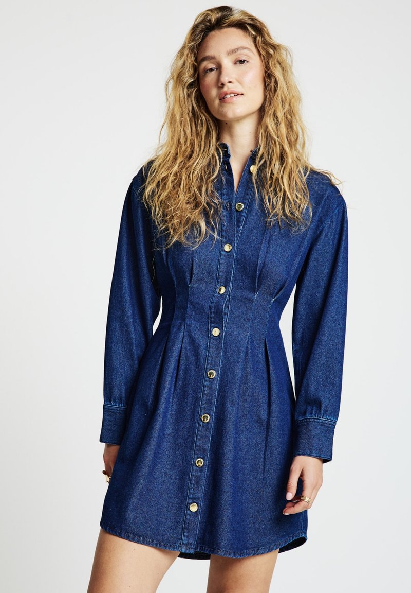 Jeanskleid mit knöpfbarer Vorderseite, goldenen Beschlägen, langen Ärmeln, tailliertem Schnitt und plissiertem Rock. Dunkelblaue Farbe mit glatter Textur.