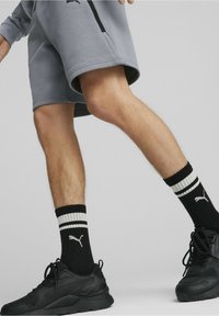 Des chaussures de sport noires, des chaussettes rayées noires et blanches, un short gris à coupe décontractée montrant le mouvement des jambes.
