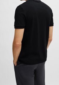 Svart kortärmad polo med en enkel krage och minimalistisk design. Mjuk tyg med slät yta. Odekorerad baksida.