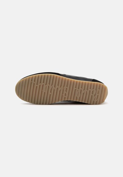 Semelle d'une chaussure noire avec une semelle extérieure en caoutchouc rainuré marron clair avec un logo de marque subtilement embossé.