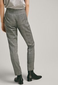 Pantalon gris à carreaux avec une coupe ajustée, doté d'une taille haute et d'une jambe slim, associé à des bottines noires.