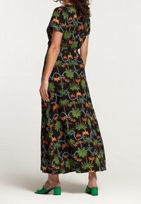 Svart maxiklänning med livfulla blomm- och bladmönster i grönt, orange och blått. Kort ärm, slät tyg, med en avslappnad silhuett.