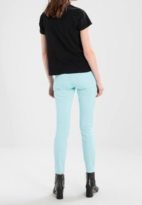 Camiseta negra de manga corta combinada con jeans skinny de color azul claro y botas negras hasta el tobillo, vista desde atrás. Diseño sencillo y forma ajustada.
