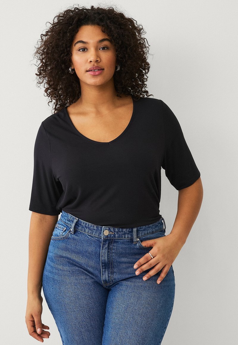 Top nero a maniche corte con scollo a V, realizzato in tessuto morbido, abbinato a jeans blu a vita alta con stile classico a cinque tasche.