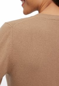 Beige gebreide trui met een ronde halslijn, voorzien van een geribde zoom en manchetten, met een gladde textuur en een naadloos schouderontwerp.