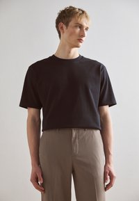 Tricou din bumbac negru, cu mâneci scurte, decolteu rotund și o croială lejeră, asociat cu pantaloni bej șablonați. Design simplu și curat.