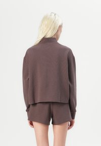 Brun teksturert cropped genser med høy krage, parret med matchende shorts. Stoffet ser mykt ut med et subtilt mønster.