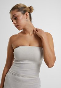 Robe grise sans bretelles en tissu texturé, mettant en avant une silhouette ajustée et une finition lisse. Le mannequin porte des boucles d'oreilles en argent.