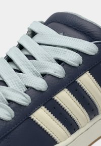 Κοντινή λήψη ενός ναυτικού μπλε αθλητικού παπουτσιού με ανοιχτό μπλε κορδόνια και τρεις κρεμ ρίγες στο πλάι.