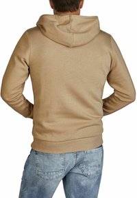 Tan hoodie with a drawstring hood, front pockets, and ribbed cuffs. Back view shows a smooth texture and fitted design, paired with light blue jeans.