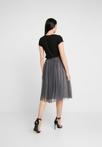 Zwarte top met korte mouwen, gecombineerd met een vloeiende grijze tule rok met een geplooide tailleband en een gelaagd ontwerp. Zwarte high-heeled sandalen.