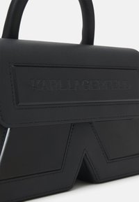 Black handbag made of smooth leather, featuring embossed logo, structured shape, and angular design details with contrasting stitching.