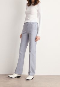 Jasnoszare rozszerzane spodnie wykonane z gładkiego materiału, z płaskim przodem, zapięciem na zamek błyskawiczny i bocznymi kieszeniami, zestawione z białymi botkami za kostkę.