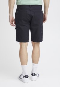 Pantalones cortos de carga en color navy con múltiples bolsillos, hechos de algodón. Presentan un corte recto, una textura suave y se llevan con calcetines blancos y zapatillas.